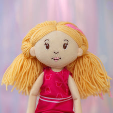 Plush doll with blonde hair and a pink dress against a blurred background