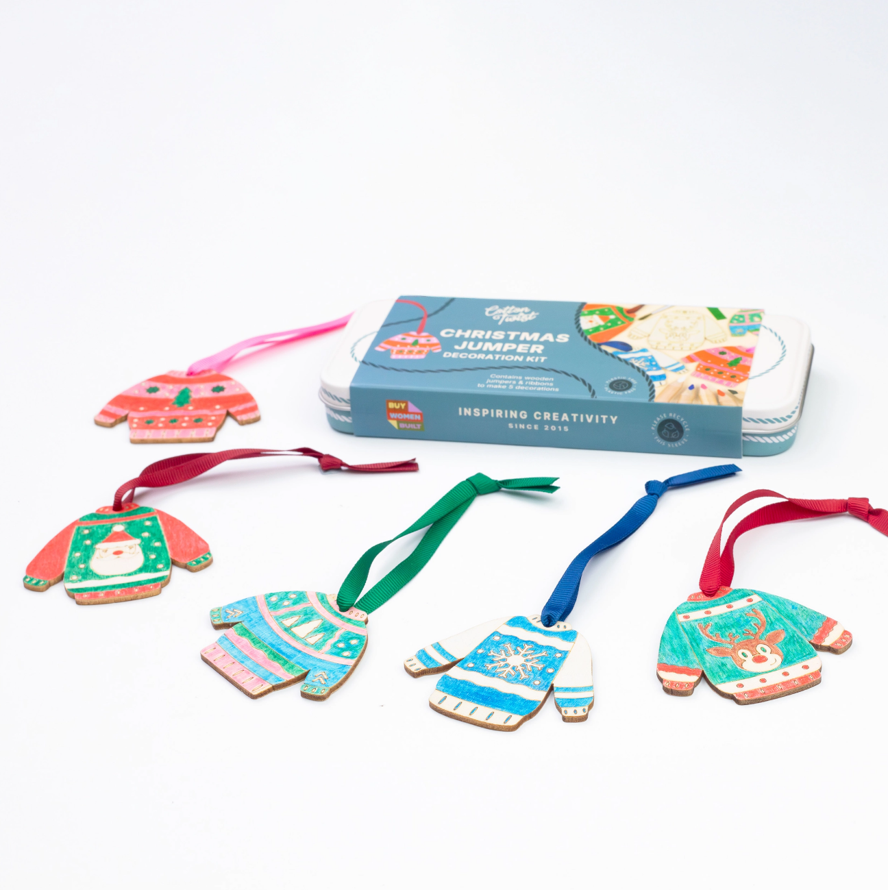 A Christmas jumper ornament kit with five colorful wooden sweater ornaments in different holiday patterns, hanging ribbons, and a blue metal tin box labeled 'Christmas Jumper' on a white background.